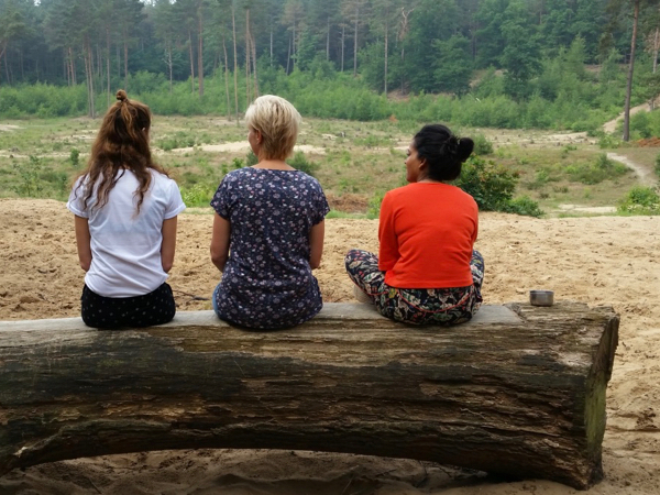 3 vrouwen zitten buiten met de rug naar je toe op een boomstam